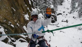 A man waving to the camera while ice climbing.